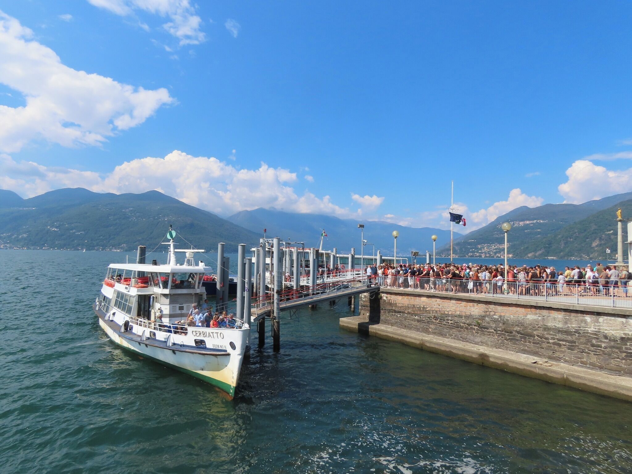 A boat docked at a pier with a crowd of people on the adjacent walkway.
