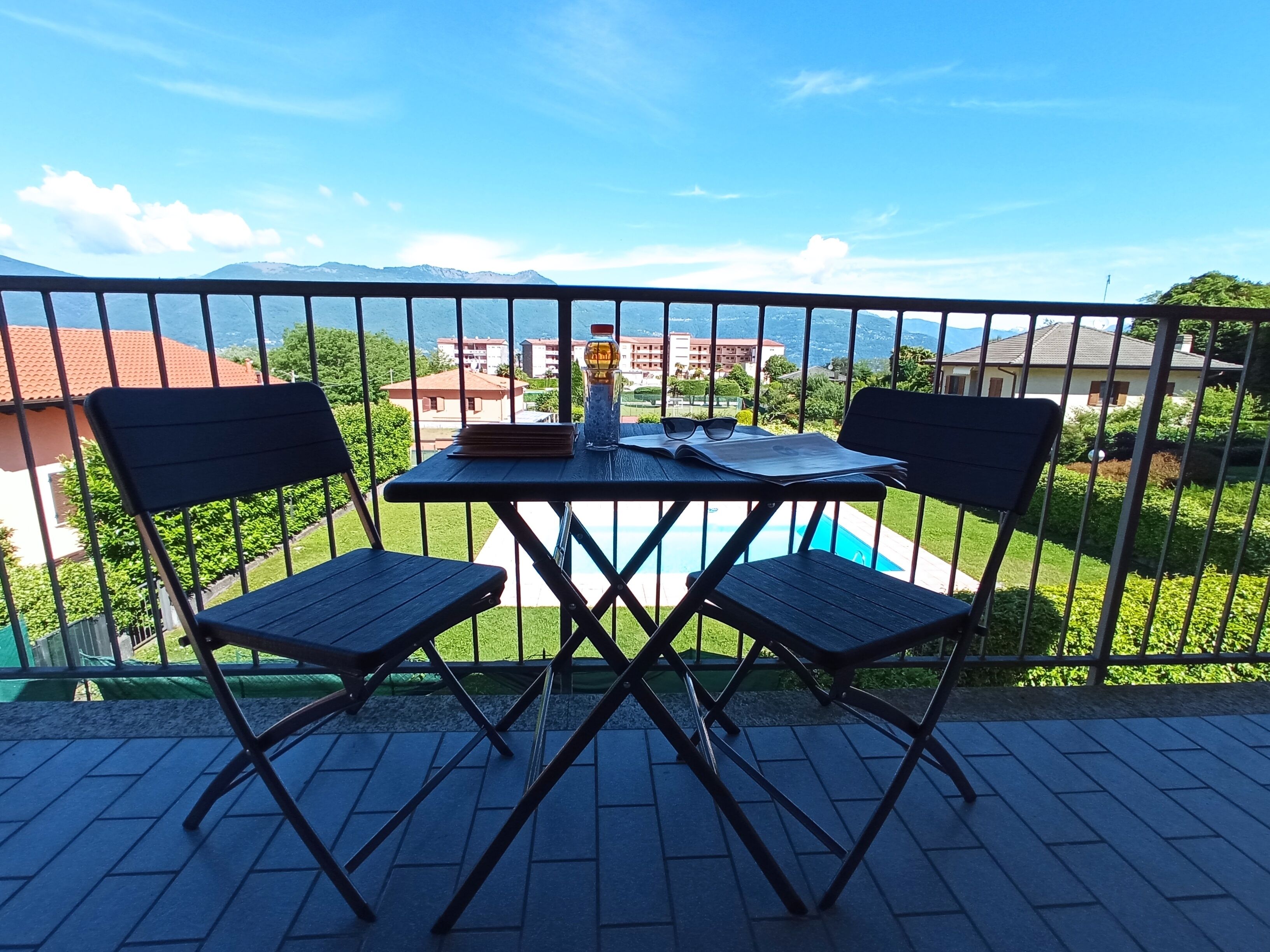 A balcony with a table and two chairs, overlooking a swimming pool and buildings.