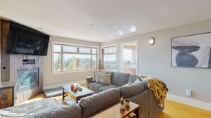 Een moderne woonkamer met een grijze bank, een houten salontafel en een aan de muur bevestigde televisie.