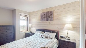 Een slaapkamer met een bed, twee nachtkastjes, een kaptafel, een raam en een aan de muur hangend schilderij.
