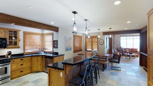 A spacious kitchen with wooden cabinets, a central island, and a dining area with bar stools. - Okanagan - Rockridge 375 Snow Escape (Kootenay Boundary E / West Bo)