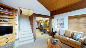 A living room with a TV, wooden staircase, and a sofa. - Okanagan - Rockridge 375 Snow Escape (Kootenay Boundary E / West Bo)