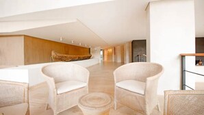 Een ruime lobby met hoge plafonds, rieten stoelen, een centraal houten sculptuur en een modern receptiebalie.