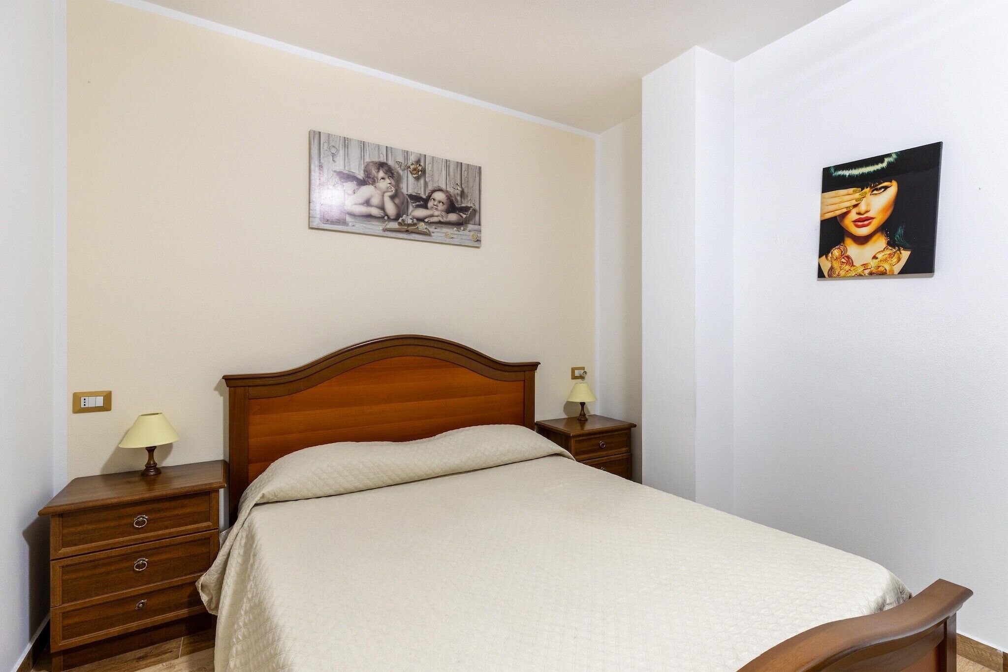 Une chambre à coucher avec un lit en bois, deux tables de chevet avec des lampes, une petite table et deux œuvres d’art accrochées au mur.