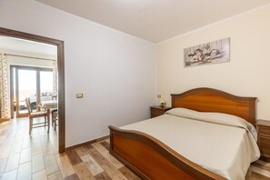 A bedroom with a wooden bed, a nightstand, a painting on the wall, and a dining area with a table and chairs.