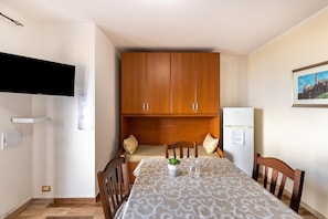 A compact kitchen with wooden cabinets, a dining table with a patterned tablecloth, and a refrigerator.