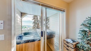 Una habitación con puerta de vidrio corrediza que da a un balcón con jacuzzi. Hay un pequeño árbol de Navidad y una cesta de mimbre en el suelo.