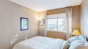 Una habitación de hotel con una cama, una ventana con cortinas, una lámpara de pared y un cuadro enmarcado.