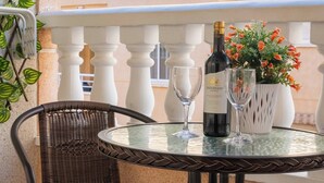 Mesa redonda con una botella de vino, una copa y una planta en maceta en un balcón con barandilla blanca.