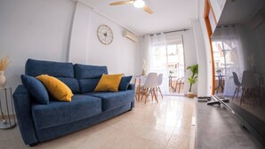 Una sala de estar moderna con un sofá azul, un ventilador de techo y un comedor con mesa y sillas.