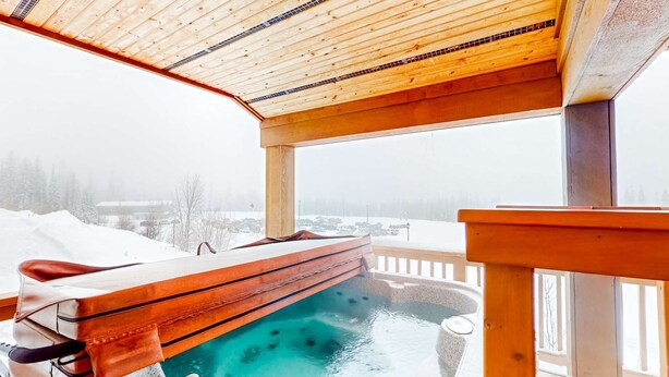 Ett spaområde i trä med ett bubbelbad, en bänk och utsikt över ett snötäckt landskap.