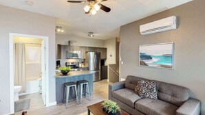 A modern living room with a gray sofa, a coffee table with a plant, and a kitchen area with stainless steel appliances. - Okanagan - Sunshine Beach (Christina Lake)
