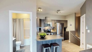 A modern kitchen with a central island, stainless steel appliances, and a small seating area. - Okanagan - Sunshine Beach (Christina Lake)