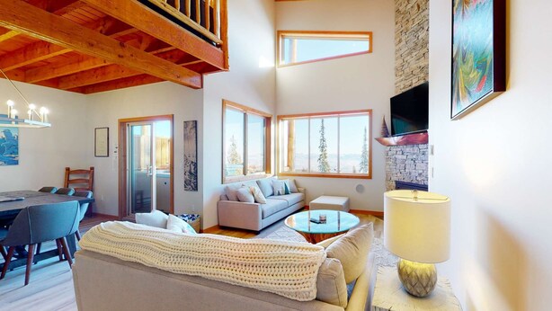 A spacious living area with a high ceiling, large windows, a fireplace, and a cozy seating arrangement. - Okanagan - Snowy Creek 10 (Beaverdell)