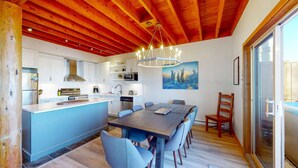 A modern kitchen with white cabinets, a central island, and a dining area with a wooden table and chairs. - Okanagan - Snowy Creek 10 (Beaverdell)