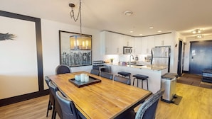 Una cocina moderna con armarios blancos, un refrigerador de acero inoxidable y una mesa de comedor de madera con sillas.
