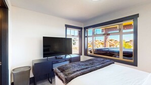 Habitación de hotel moderna con una cama grande, televisor de pantalla plana, escritorio y ventana con vista a edificios.