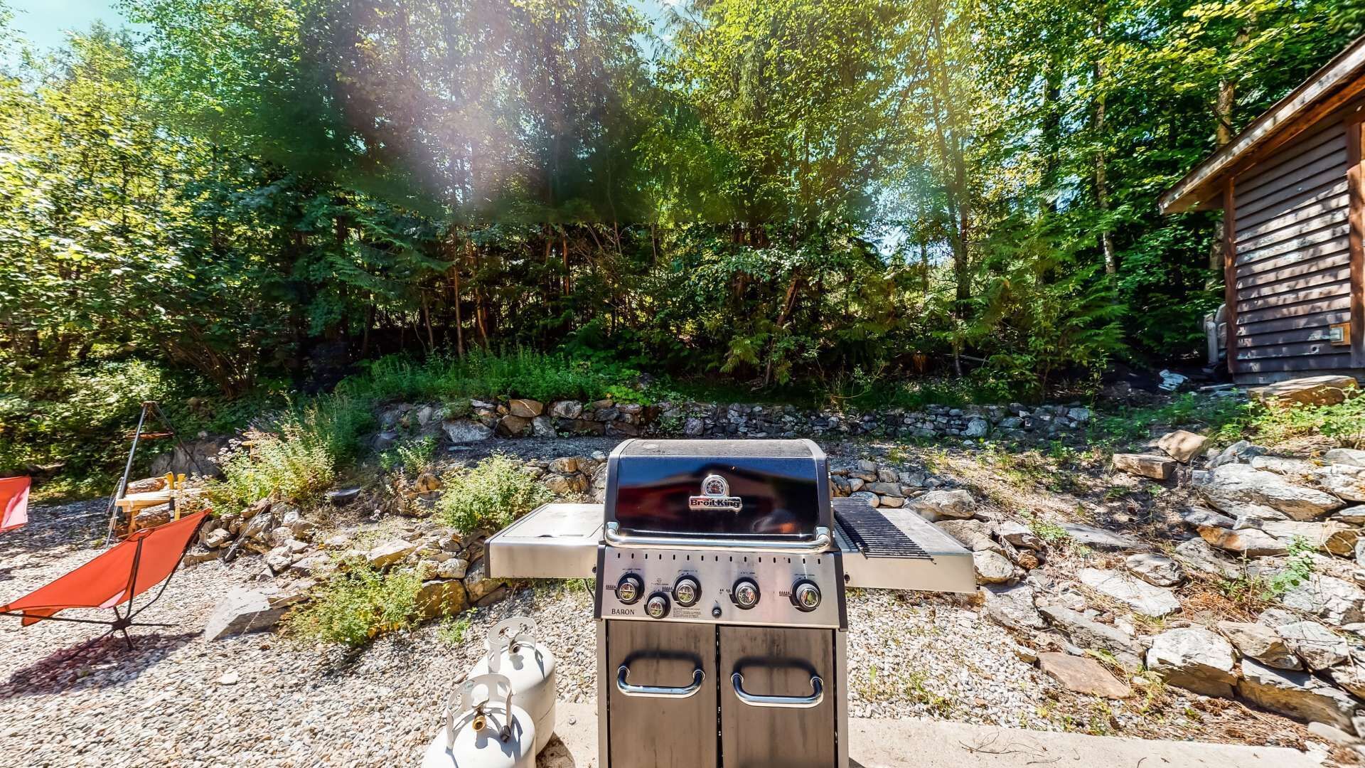 An outdoor grill area with a stone wall and trees in the background.
