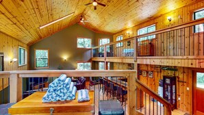 Une cabane en bois spacieuse, à plusieurs niveaux, dotée de grandes fenêtres et d’un coin salon confortable avec une table et des chaises.