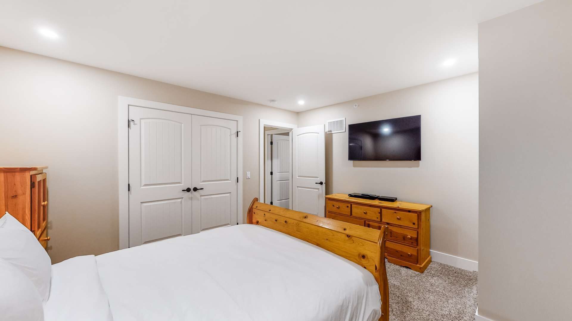 A bedroom with a bed, a wooden dresser, a TV, and a wardrobe.
