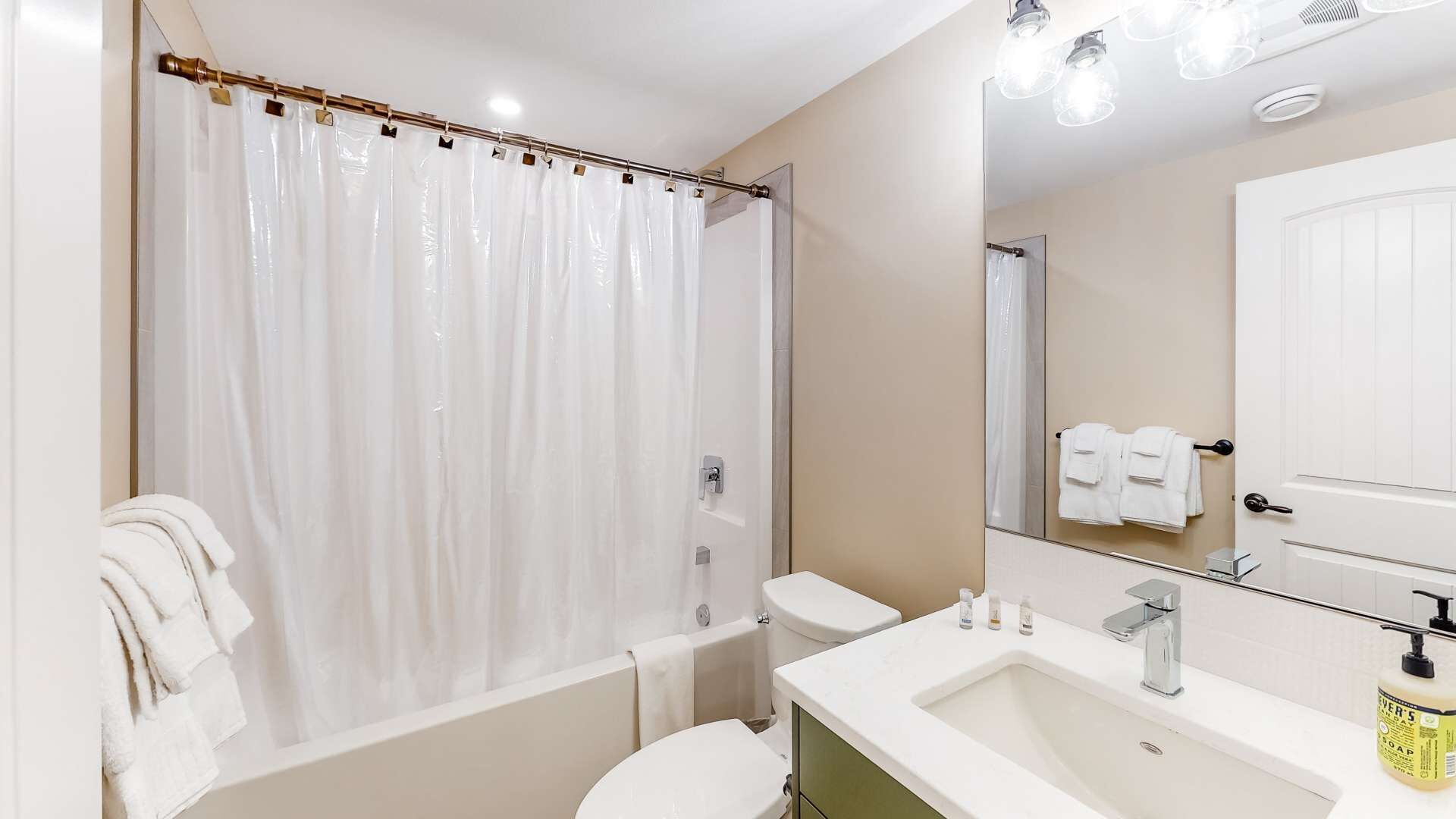 Ein modernes Badezimmer mit Duschvorhang, Toilette, Waschbecken und einem Spiegel mit Handtuchhalter.