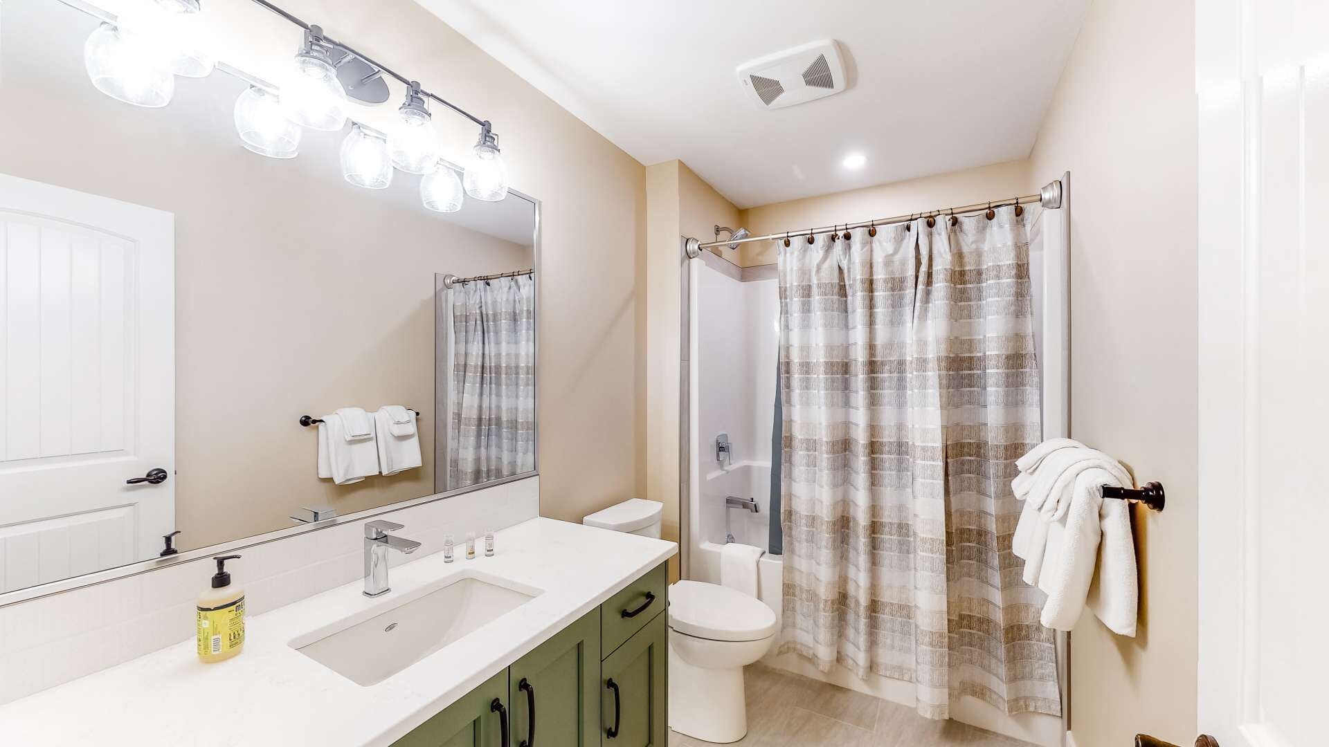 A bathroom with a white sink, mirror, and toilet. There are towels hanging on the wall and a shower curtain.
