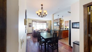 A spacious dining area with a long table and chairs, a kitchen with a stone backsplash, and a chandelier. - Okanagan - The Crescent 104 (Beaverdell)