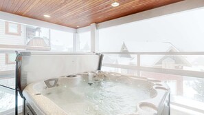 Un bain à remous dans une pièce dotée d’un plafond en bois et de grandes fenêtres.