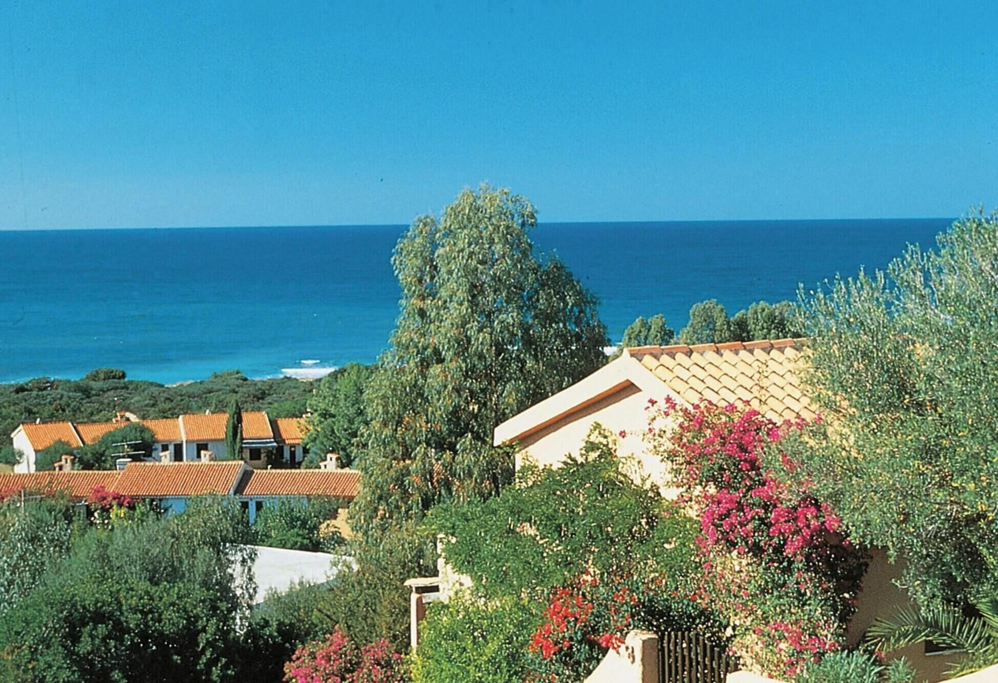 A coastal residential area with houses, a clear blue sky, and the sea in the background.