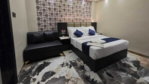 Una habitación de hotel moderna con una cama grande, un sofá de cuero negro, una mesita de noche y una pared con estampado.