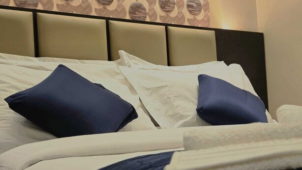 Una cama bien hecha con ropa de cama blanca y azul marino, un cabecero con diseño geométrico y una pared con estampado floral.