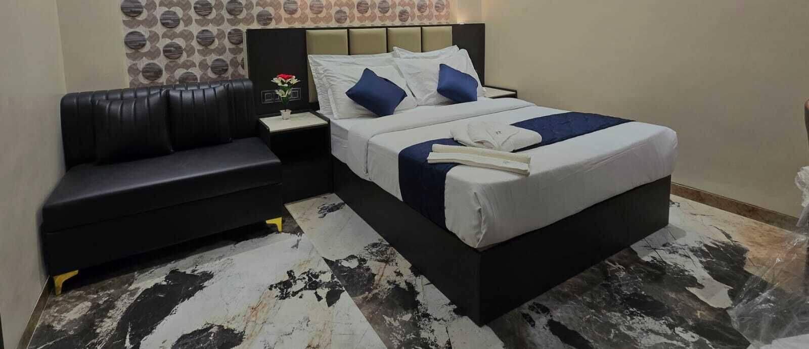 A hotel room with a bed, a black sofa, a nightstand with a vase of flowers, and a patterned wall.