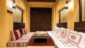 A traditional Moroccan room with a wooden door, a low sofa with patterned cushions, and a small table with a tissue box. - Heritage 2-bedroom Apartment (Dubai)