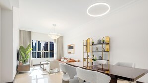 A modern living room with a dining area, large windows, and a view of tall buildings. - LUX The 02 Residences JLT Suite (Dubai)