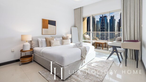 A modern hotel room with a large bed, a city view, a small table, and a chair. - LUX The 02 Residences JLT Suite (Dubai)