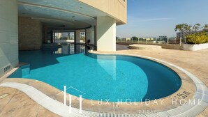 A swimming pool area with a view of the city skyline, a covered seating area, and a clear sky. - LUX The 02 Residences JLT Suite (Dubai)
