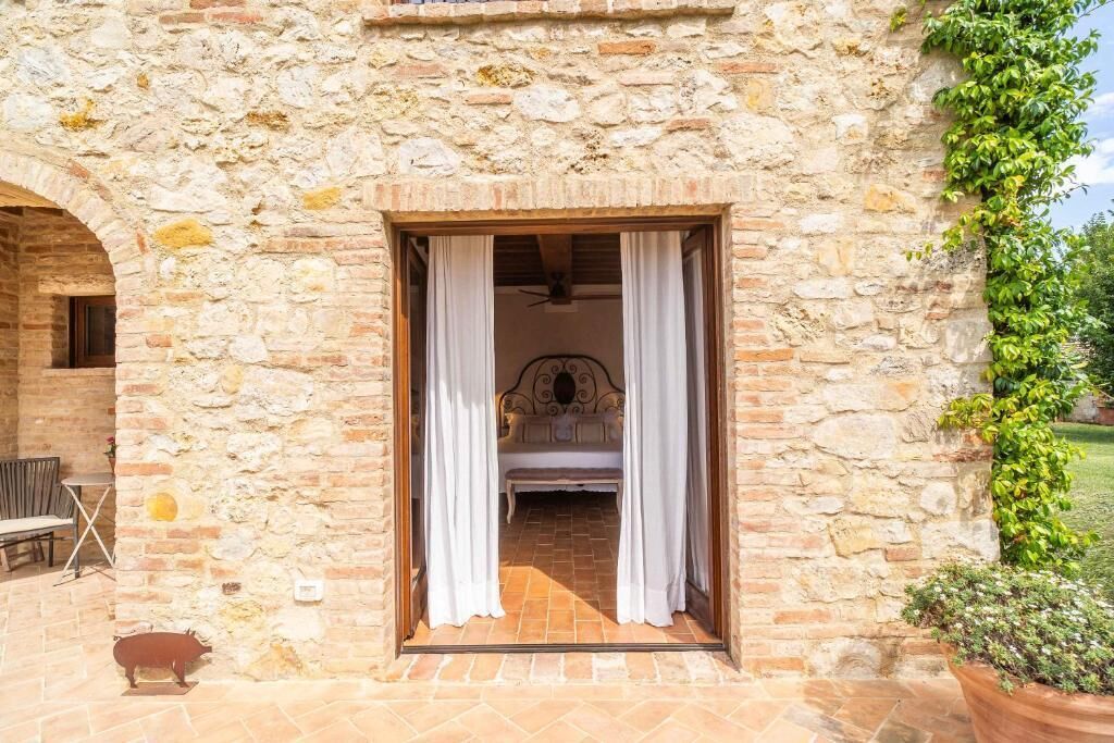 A stone building with a bedroom visible through a doorway, a bench, and a pig sculpture.