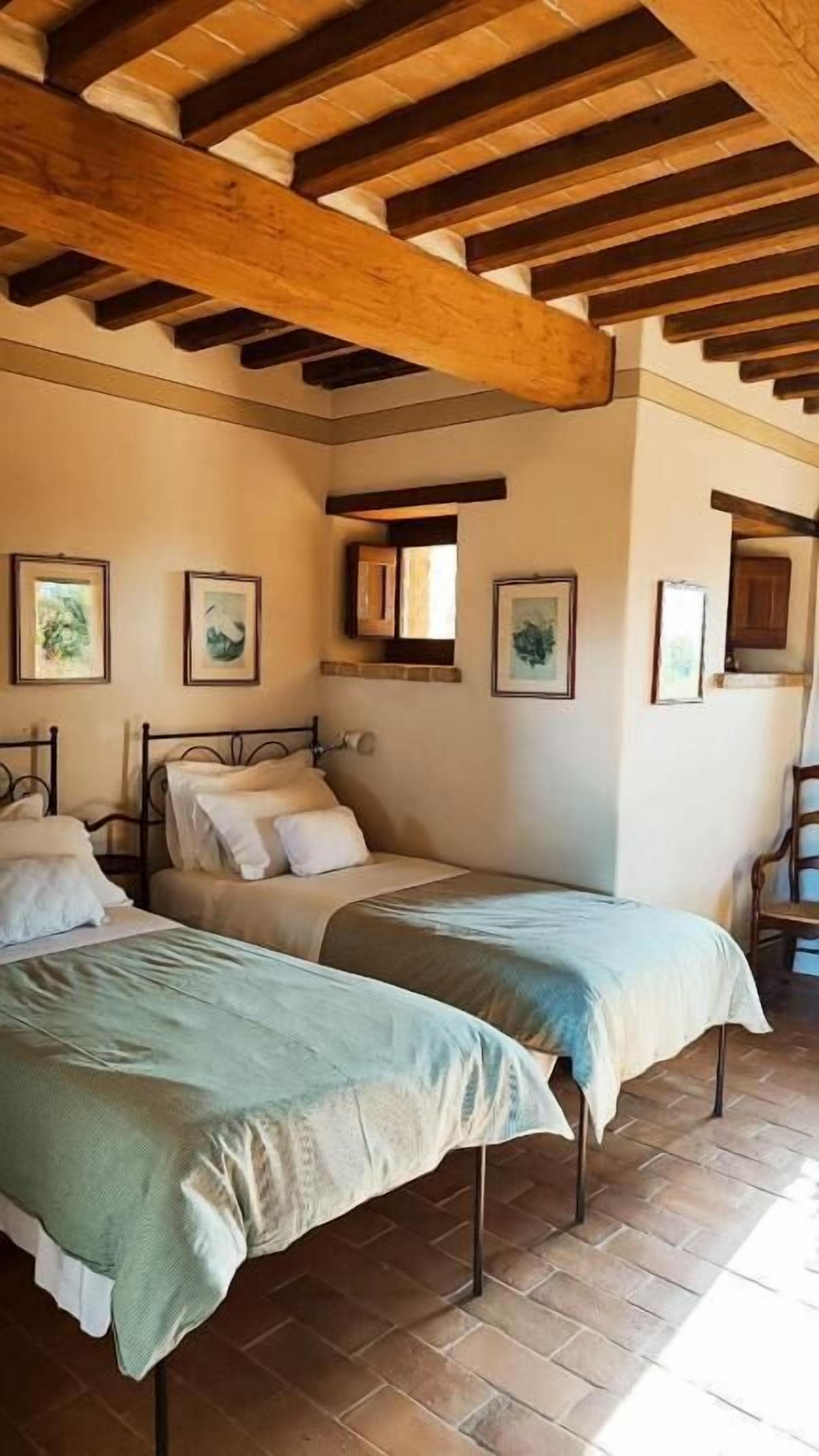 A bedroom with two beds, wooden beams on the ceiling, and framed artwork on the walls.