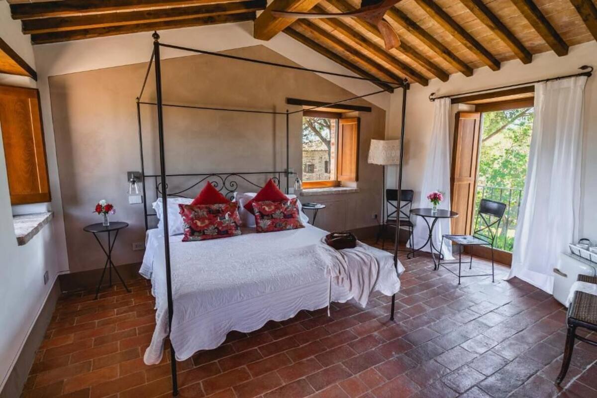 A bedroom with a four-poster bed, a small table, a chair, and a window with curtains.