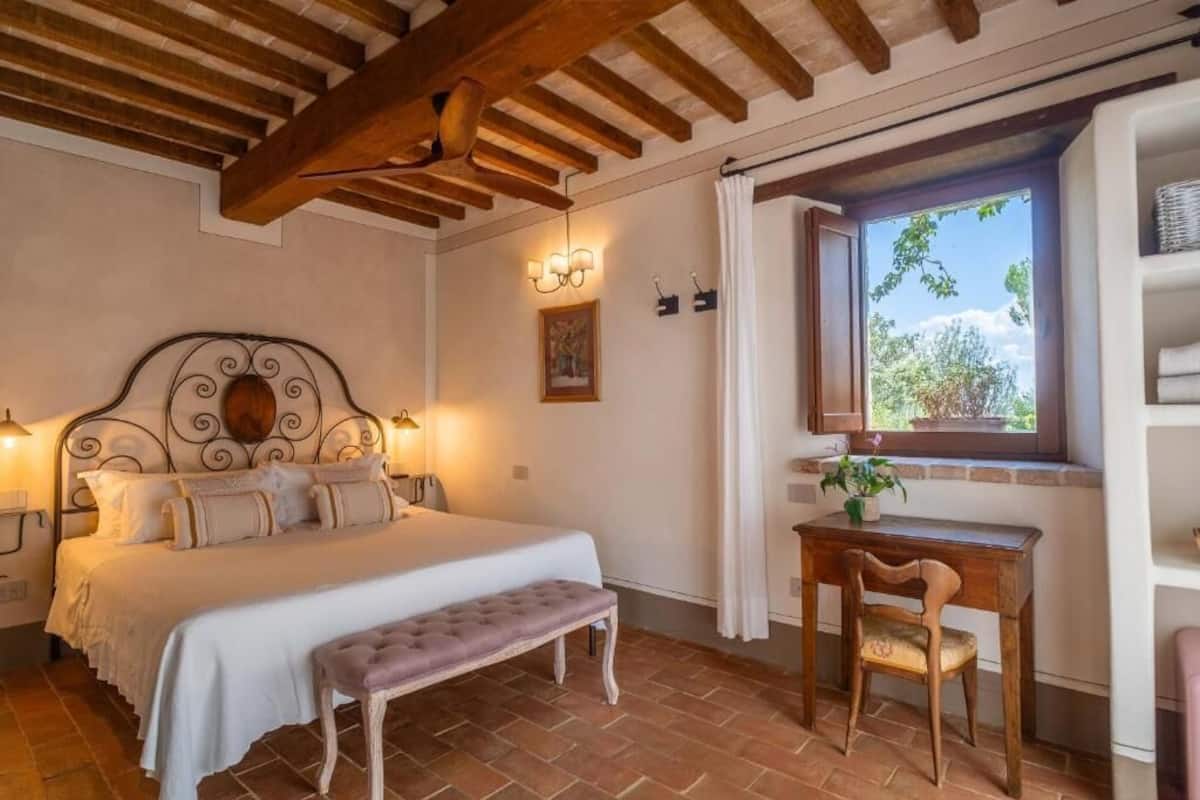 A bedroom with a bed, bench, desk, chair, and a window with a view.
