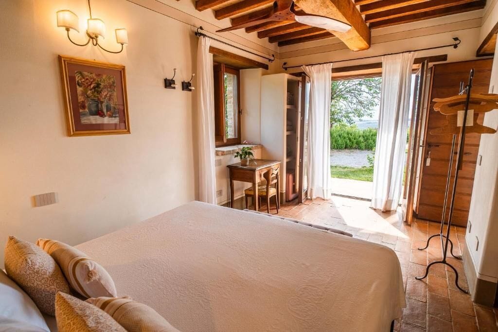 A bedroom with a large bed, a desk, and a view of the outdoors.