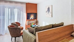 Ein modernes Wohnzimmer mit einer Couch, Sesseln, einem Fernseher und einem Bild an der Wand.