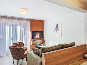 Ein modernes Wohnzimmer mit einer Couch, Sesseln, einem Fernseher und einem Bild an der Wand.