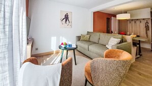 Ein modernes Wohnzimmer mit einer Couch, zwei Sesseln, einem kleinen Tisch mit einer Obstschale und einem Gemälde an der Wand.