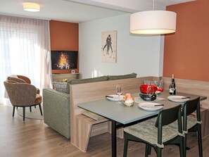 A modern living room with a dining area, featuring a sofa, chairs, a TV, and a table set for dining. - Nice apartment for 4 guests with WIFI, TV and balcony (Zermatt)