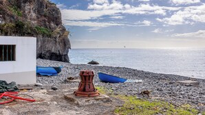 Una playa rocosa con barcos, una estructura roja y un acantilado.
