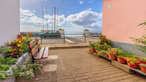 Un sendero pavimentado conduce a un banco flanqueado por macetas con plantas, con vistas a una calle y un cuerpo de agua.