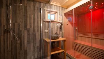 Een moderne badkamer met een houten wand, een glazen douchecabine, een houten wastafel met een stenen wasbak en een sauna met rode verlichting.