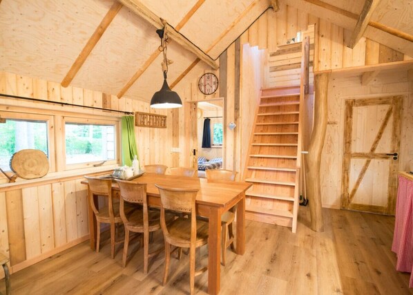 A wooden interior with a dining area, a staircase, and a clock on the wall.