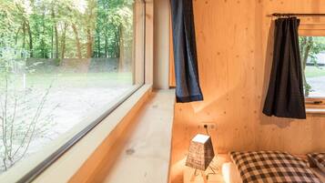 Een houten kamer met een bed, een tafeltje en een raam met uitzicht op een bos.